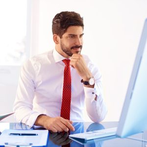 Portrait shot of thinking young businessman wearing shirt and tie while sitting in front of laptop and working on new project.